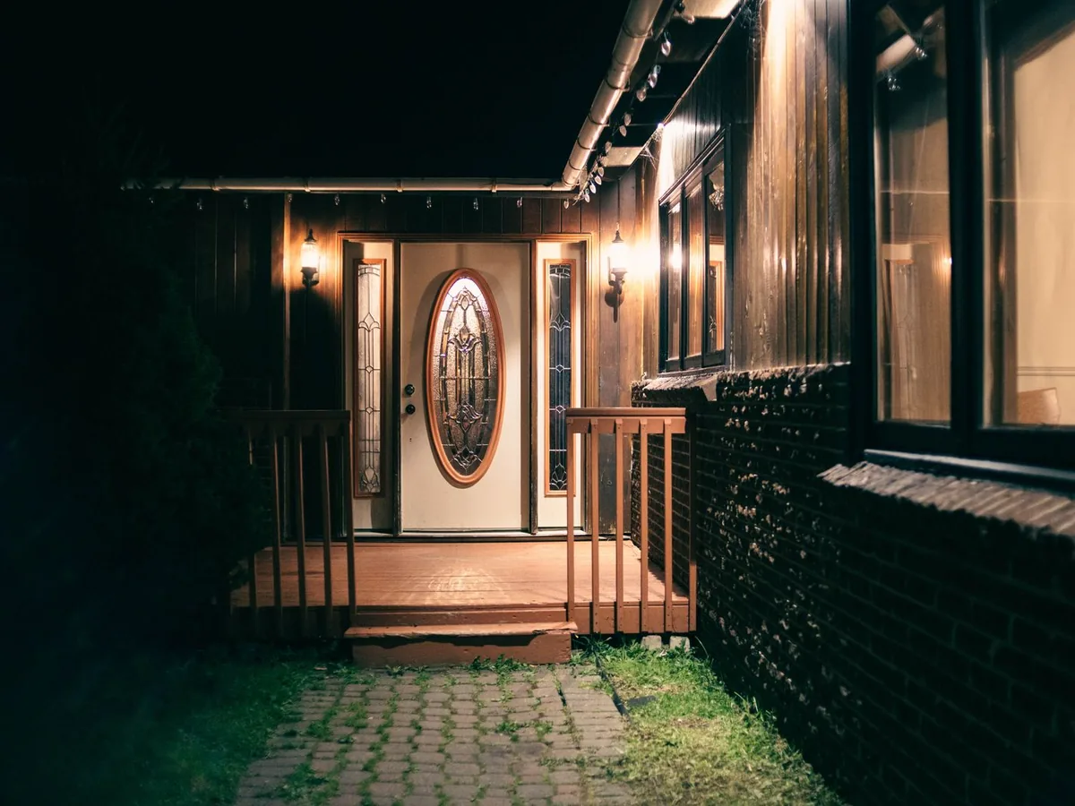 Front porch of a house at night with the lights on beside the front door